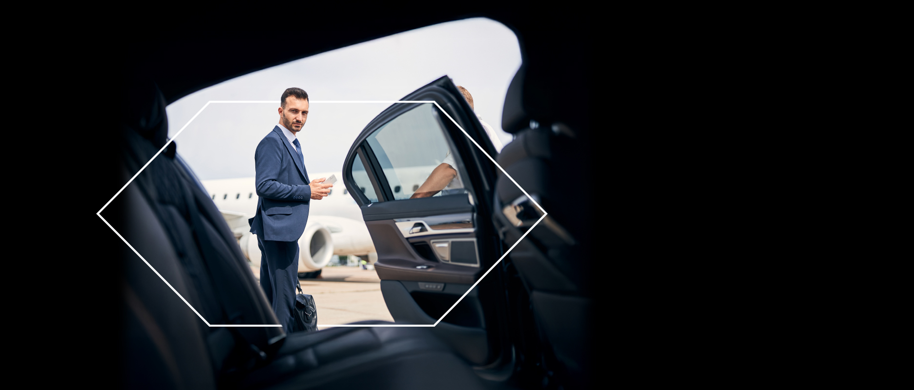 رجل يرتدي بدلة ينظر داخل سيارة فاخرة بابها مفتوح وطائرة خاصة في الخلفية