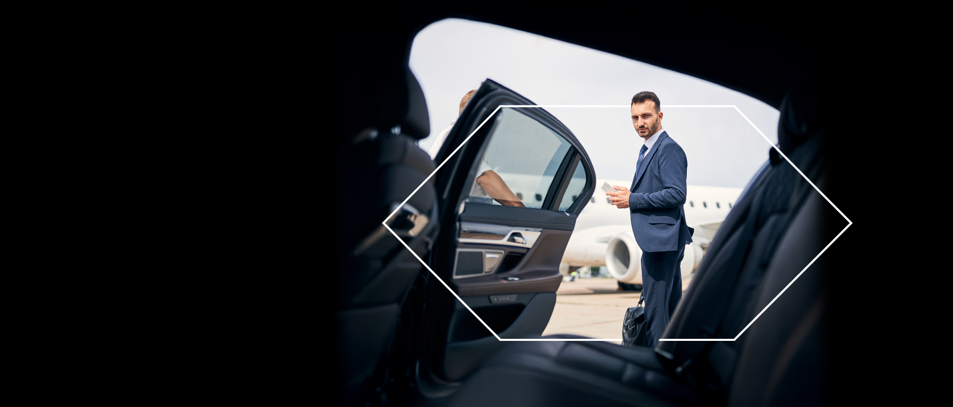 a man wearing a suit looking inside a luxury car with the car door open and a private jet in the background