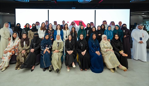 The image shows a large group of men and women standing and sitting together in a modern hall, posing for a formal group photo.